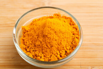 Turmeric powder in glass bowl on wooden background.