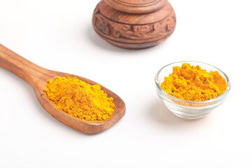 Turmeric powder in wooden spoon and glass bowl on white background.
