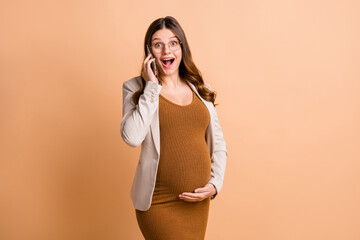 Photo of pretty excited woman expecting child wear jacket arm belly talking modern device isolated beige color background