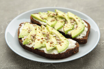 Avocado sandwich on dark rye bread made with fresh sliced avocados on grey background.