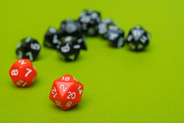 Many black and two red dices fell out of the dice container on a green background: dice D20, D10, D12, D8, D6 with space for text, side view, concept of role-playing games and games
