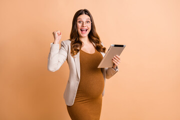 Photo of cute lucky woman expecting child wear jacket belly holding modern gadget rising fist isolated beige color background