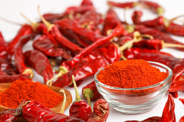 Dried red chilli and powder in glass bowl on white background.