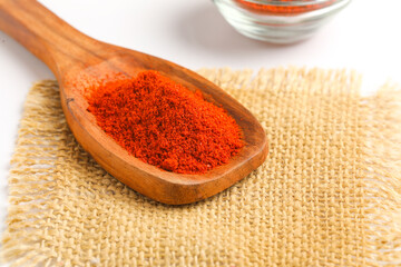 close view of red chilli powder in wooden spoon on white background.