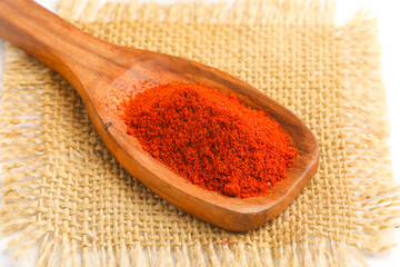 close view of red chilli powder in wooden spoon on white background.
