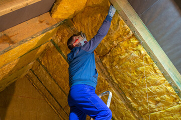 The man insulates the attic of the house with mineral wool - obrazy, fototapety, plakaty