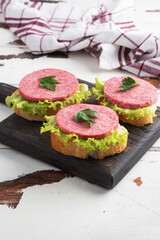 Sandwiches with lettuce leaves and sliced salami sausage on a wooden Board. Copy space