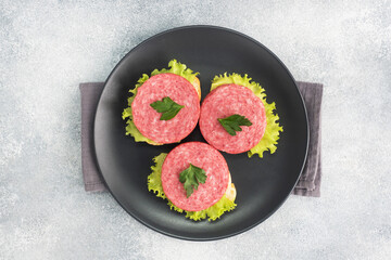Sandwiches with lettuce leaves and sliced salami sausage on black plate. Copy space top view