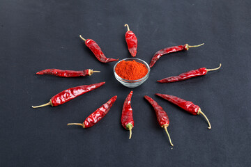 Dried red chilli and powder in glass bowl on dark background.