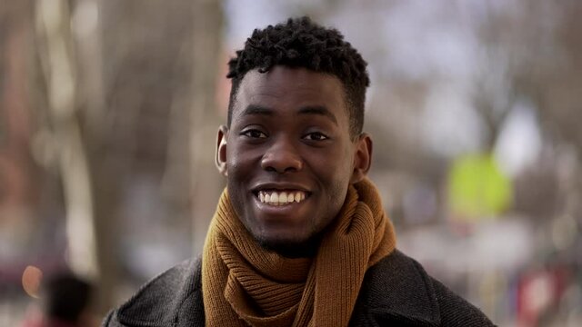 Friendly black african man portrait smiling at camera standing outdoors in urban city wearing scar furing cold season