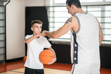 Coach in white sportswear and a boy with a ball in the gym