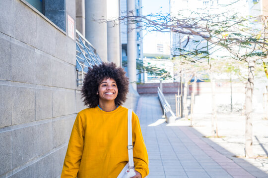 Close up portrait of beautiful young black woman smiling outdoors in the street of a grey city - businesswoman walking and having fun alone
