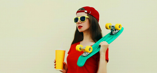 Fototapeta premium Summer portrait of young woman with cup of juice and green skateboard wearing a red baseball cap