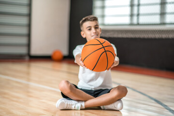 Naklejka premium A dark-haired boy sitting on the floor and holding a ball in hands