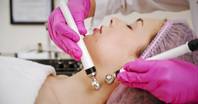 Beautiful woman receiving facial microcurrent treatment at spa salon. Beautician using electrical impulses for facial procedures. Woman in spa salon.