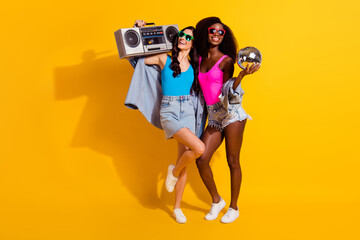 Photo of two ladies hold disco ball recorder look empty space wear sunglass jeans outfit isolated...