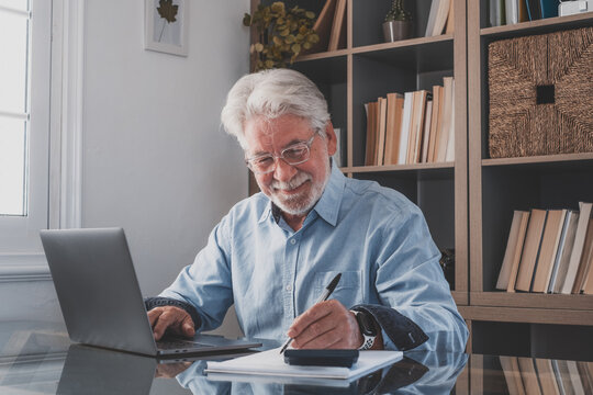 Happy old caucasian businessman smiling working online watching webinar podcast on laptop and learning education course conference calling make notes sit at work desk, elearning concept.