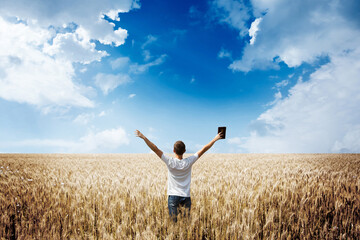 Naklejka na ściany i meble Man holding up Bible in a wheat field