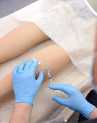 The doctor injects a syringe under the knee. A doctor makes an injection to the varicose veins on a woman s leg, close-up, sclerotherapy, stripping, phlebeurysm, medical.
