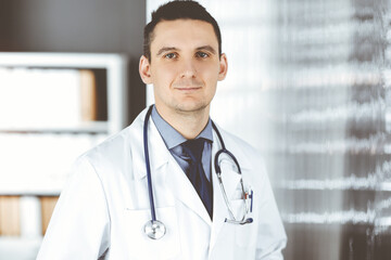 Male doctor standing straight in clinic near his working place. Perfect medical service in hospital. Medicine and healthcare concept