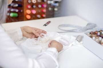 Obraz na płótnie Canvas Woman hands sewing decor to white clothes