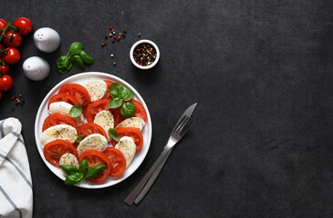 Fototapeta na wymiar Caprese is a tomato and mozzarella appetizer. Traditional Italian salad on a concrete background with space for text.