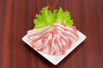 Sliced uncooked streaky bacon with lettuce on square dish