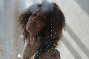 Sensual portrait of young woman taking a shower. Defocused female looks through the glass of the shower stall.