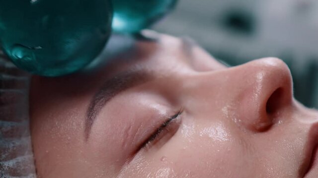 Face massage with glass balls. The beautician runs glass spheres over the face of a young woman. Extreme close-up.
