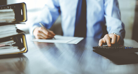 Unknown man accountant in blue shirt use calculator and computer with holding pen on while staying...