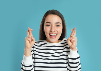 Woman with crossed fingers on light blue background. Superstition concept