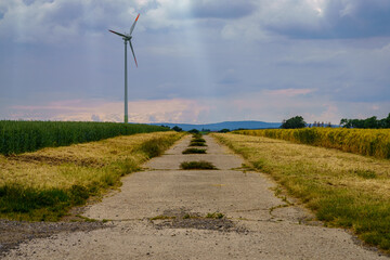 Fototapeta na wymiar A rural road through the fields with a wind wheel near Altenhagen, Lower Saxony, Germany