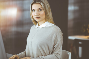 Blonde business woman sitting and looking at camera in sunny office