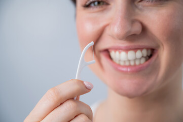 Close-up portrait of a beautiful caucasian woman with a flawless smile holding a toothpick with dental floss on a white background