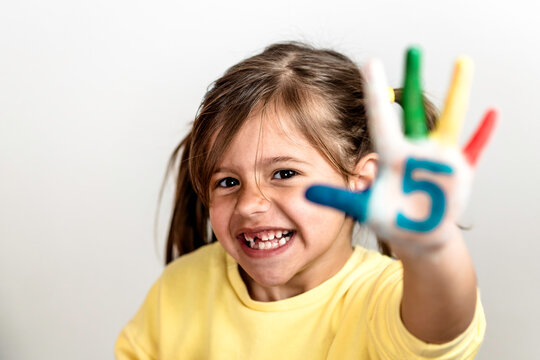 Happy toothless little girl with the five number painted on the hand laughing and having fun - Little girl who is painting her hands with numbers - The number five and childhood concept