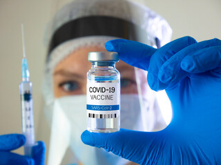 Doctor holds COVID-19 vaccine and syringe in hand. Doctor looks at the coronavirus vaccine. Woman doctor face.