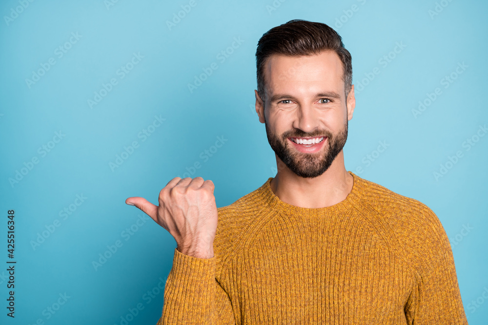 Sticker photo of young happy smiling positive cheerful handsome man point thumb in copyspace isolated on blu