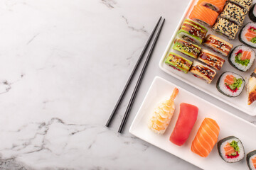 Sushi rolls set served on a white stone background and chopsticks on the side. Traditional Japanese food, top view, copy space.