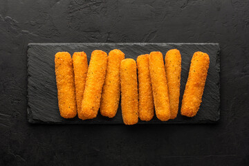 Cheese sticks set on a slate board, top view, black rustic background.