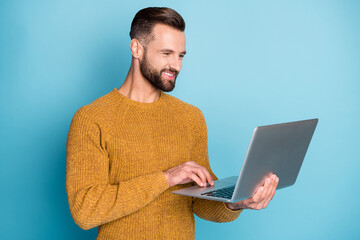 Portrait of nice attractive focused cheerful guy employee using laptop programming isolated over bright blue color background