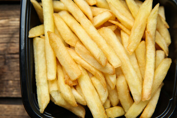Container with French fries on wooden table, top view. Food delivery service