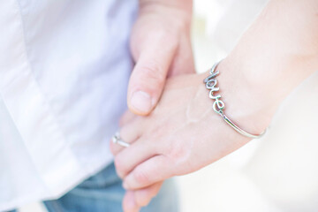 close-up of a man's hand holding a woman's hand in a bracelet with the inscription love