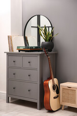 Stylish turntable, guitar and vinyl records on chest of drawers indoors