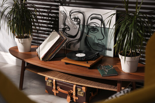 Stylish turntable with vinyl discs on table in room