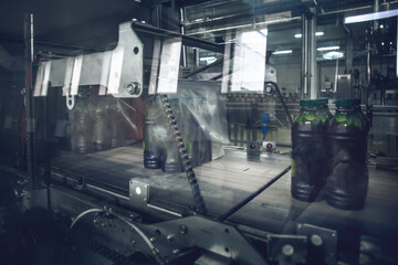 Fototapeta na wymiar Process of packaging juice bottles into plastic on automatic beverage production line. Final stage of production liquid drinking goods.