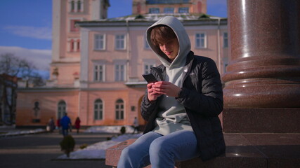 Obraz na płótnie Canvas Young man in the hood texting on cell phone, looking around