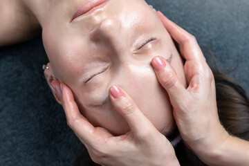 Close-up beautician doctor hand making anti-age wrinkles facial massage procedure applying lotion to attractive adult female client at beauty clinic. Cosmetologist do skincare. Healthcare therapy