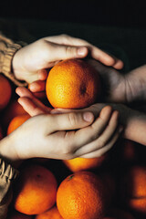 Orange in the hands of children on a dark background.