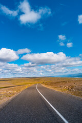 Highland landscape in Iceland, with paved asphalt road at summer sunny day and blue sky with clouds.