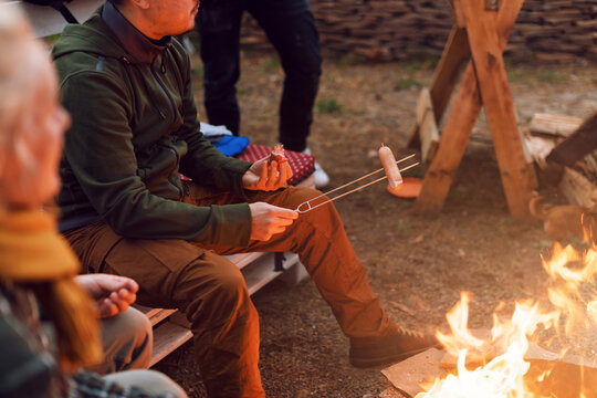 Grilling sausages over a campfire, campers roasting sausages on toasting forks. Fire place, friends,